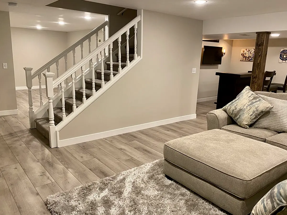 A large basement with luxury vinyl plank flooring, a wet bar, a gray couch, and recessed lighting fixtures