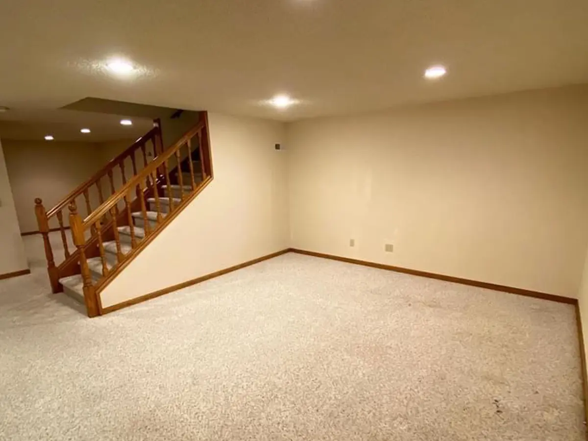 An empty basement with carpet flooring and beige walls