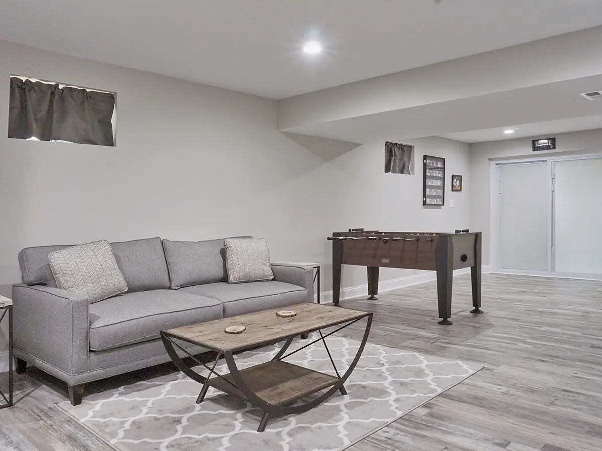 A large basement with luxury vinyl plank flooring, a couch, and a foosball table