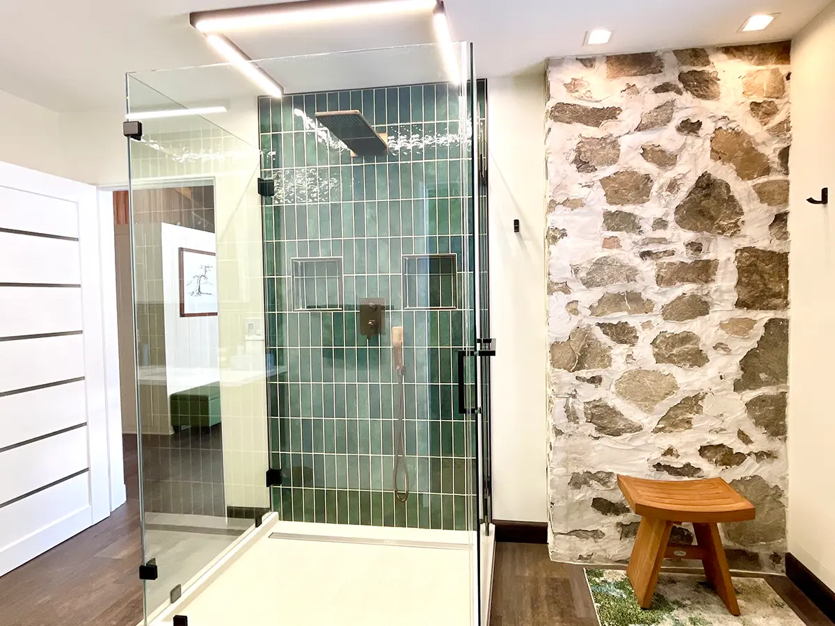 A masonry wall in a bathroom with a walk-in shower with a glass enclosure and green tile backsplash