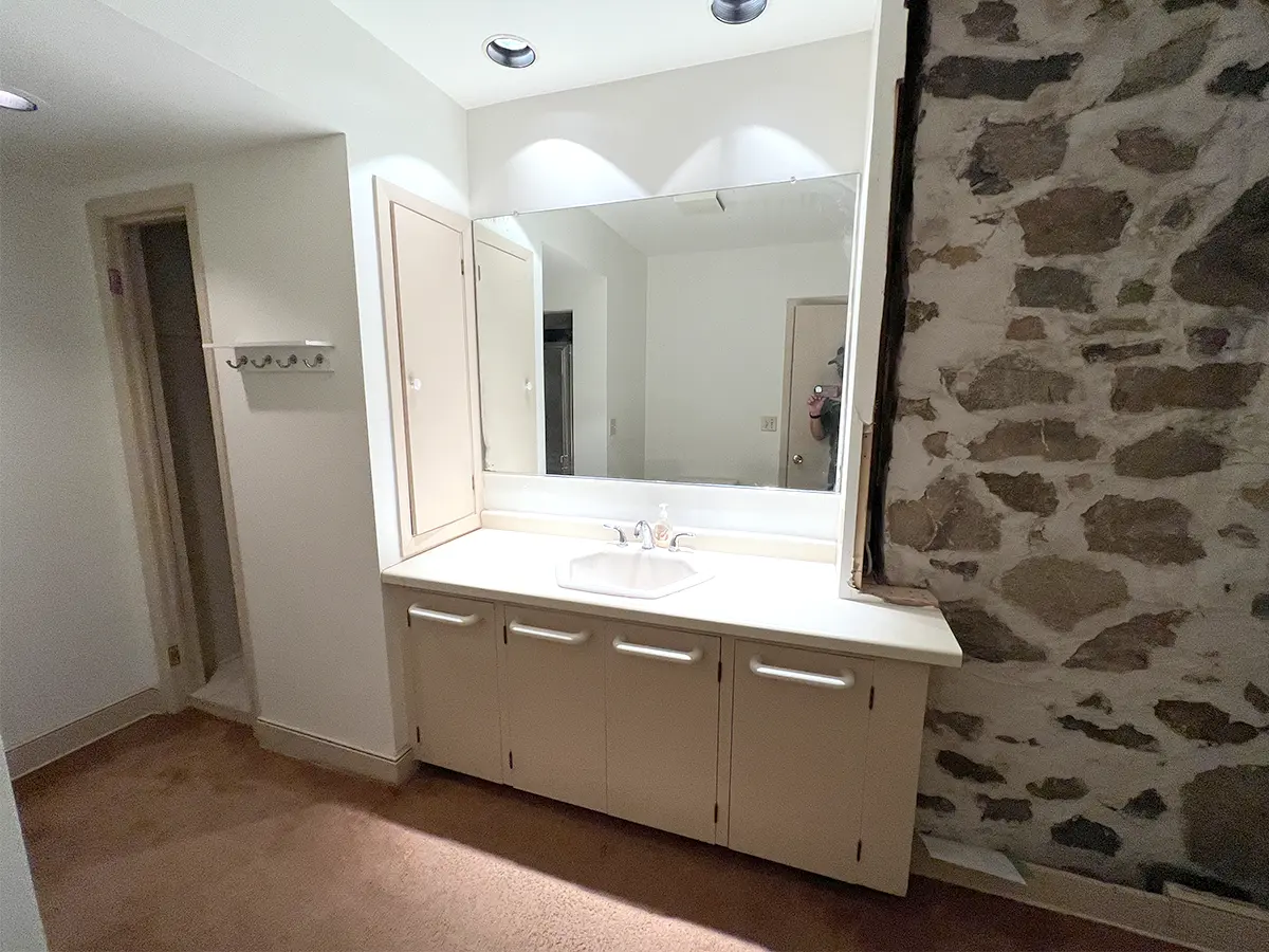 Before bathroom renovation: A masonry wall in a bathroom with a large, dated vanity