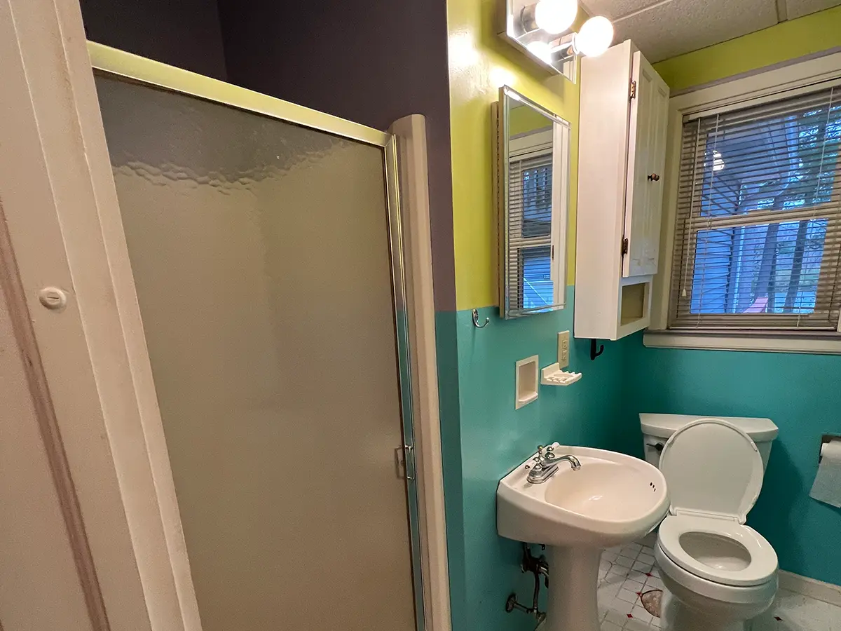 a dated bathroom with blue and green walls and an opaque shower door