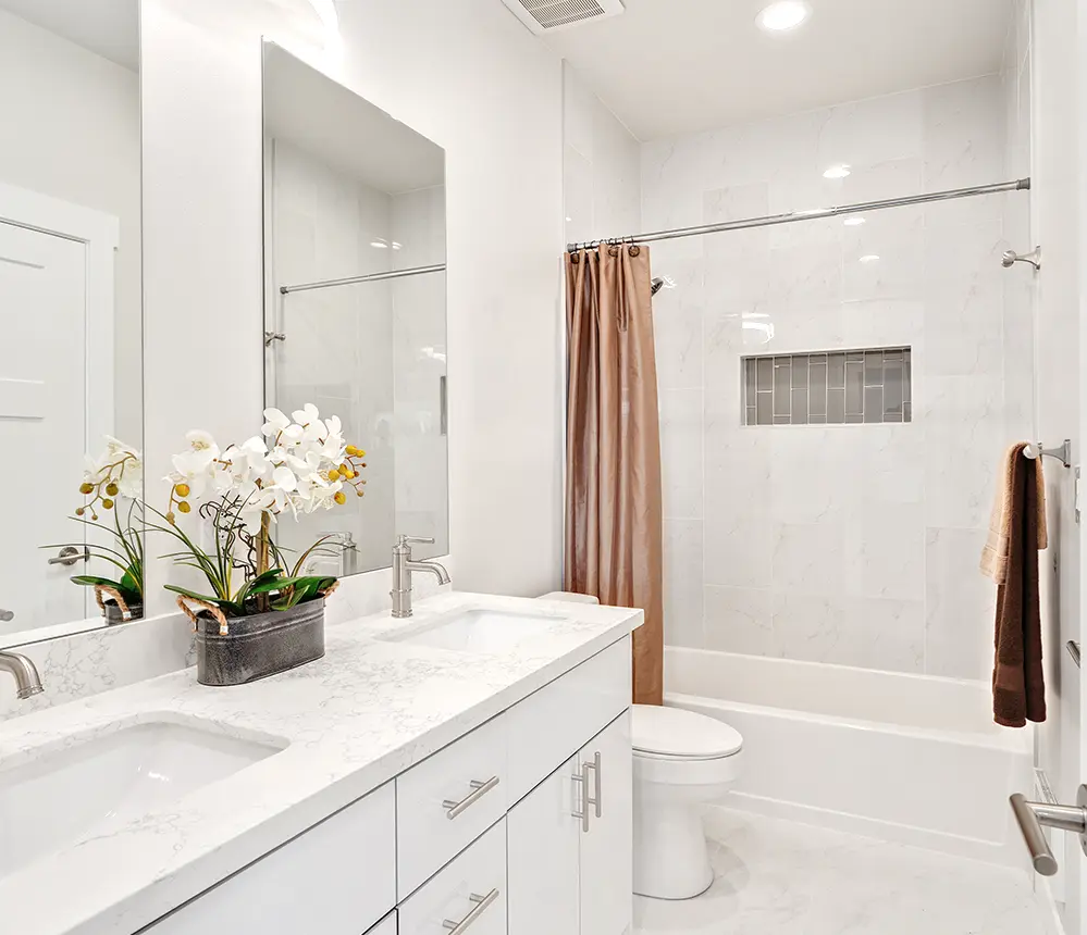 A small bathroom with a tub and shower combo, an orange shower curtain, and a quartz top with a flower on top of it