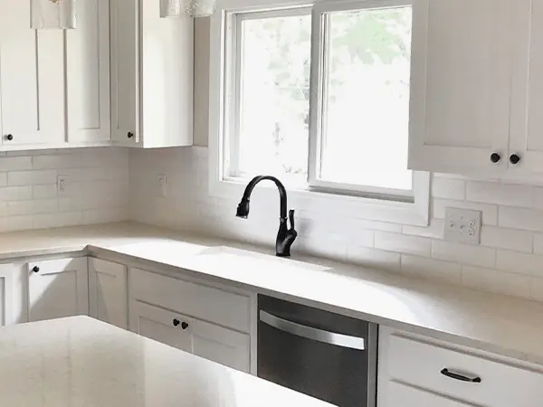 A black faucet in an all white kitchen
