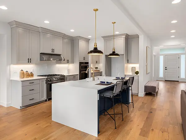 Hardwood flooring in an open space kitchen with gray cabinets and overhang lights