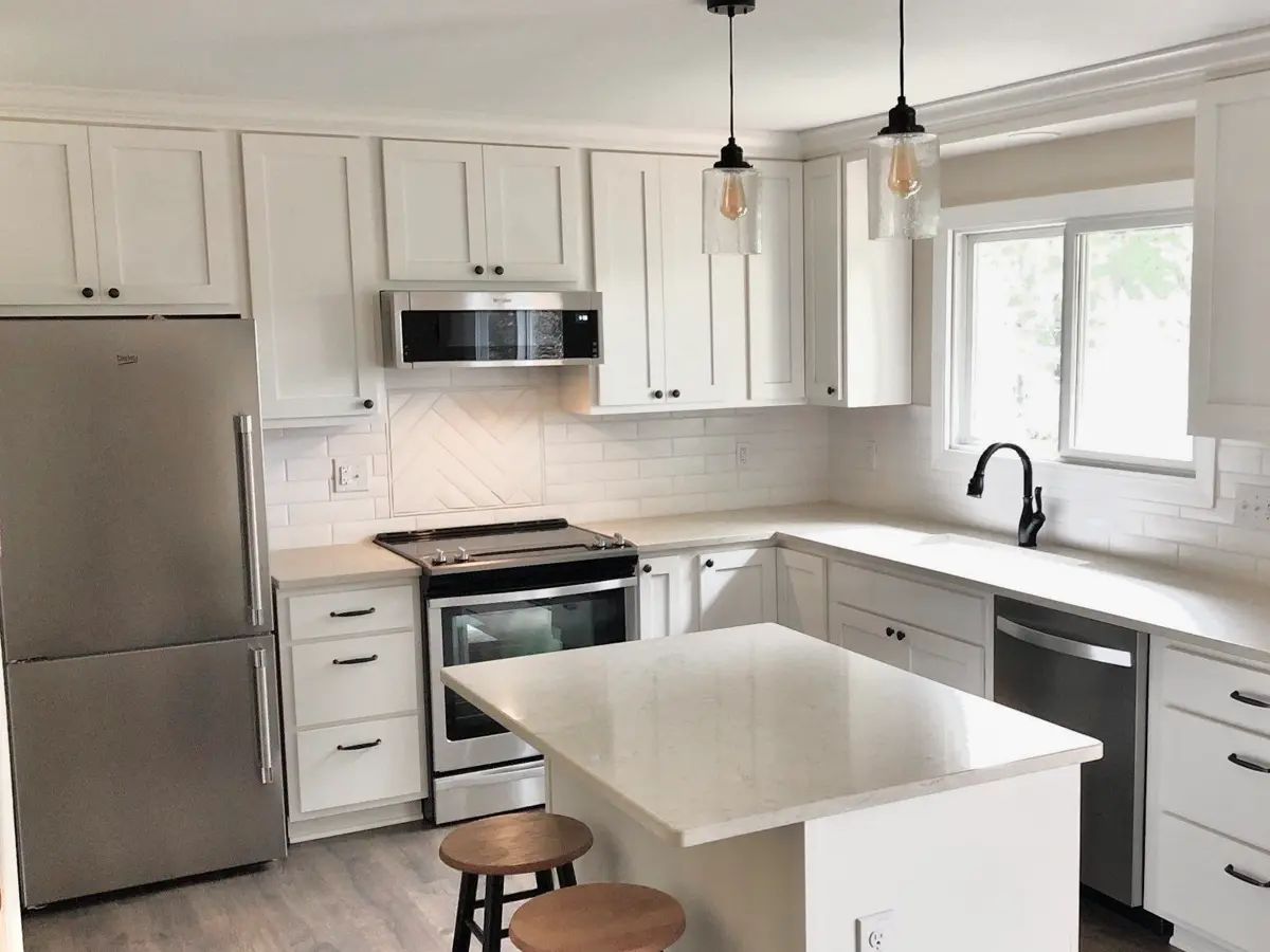 White kitchen cabinets with black pulls and knobs, a small island, and pendant lighting fixtures