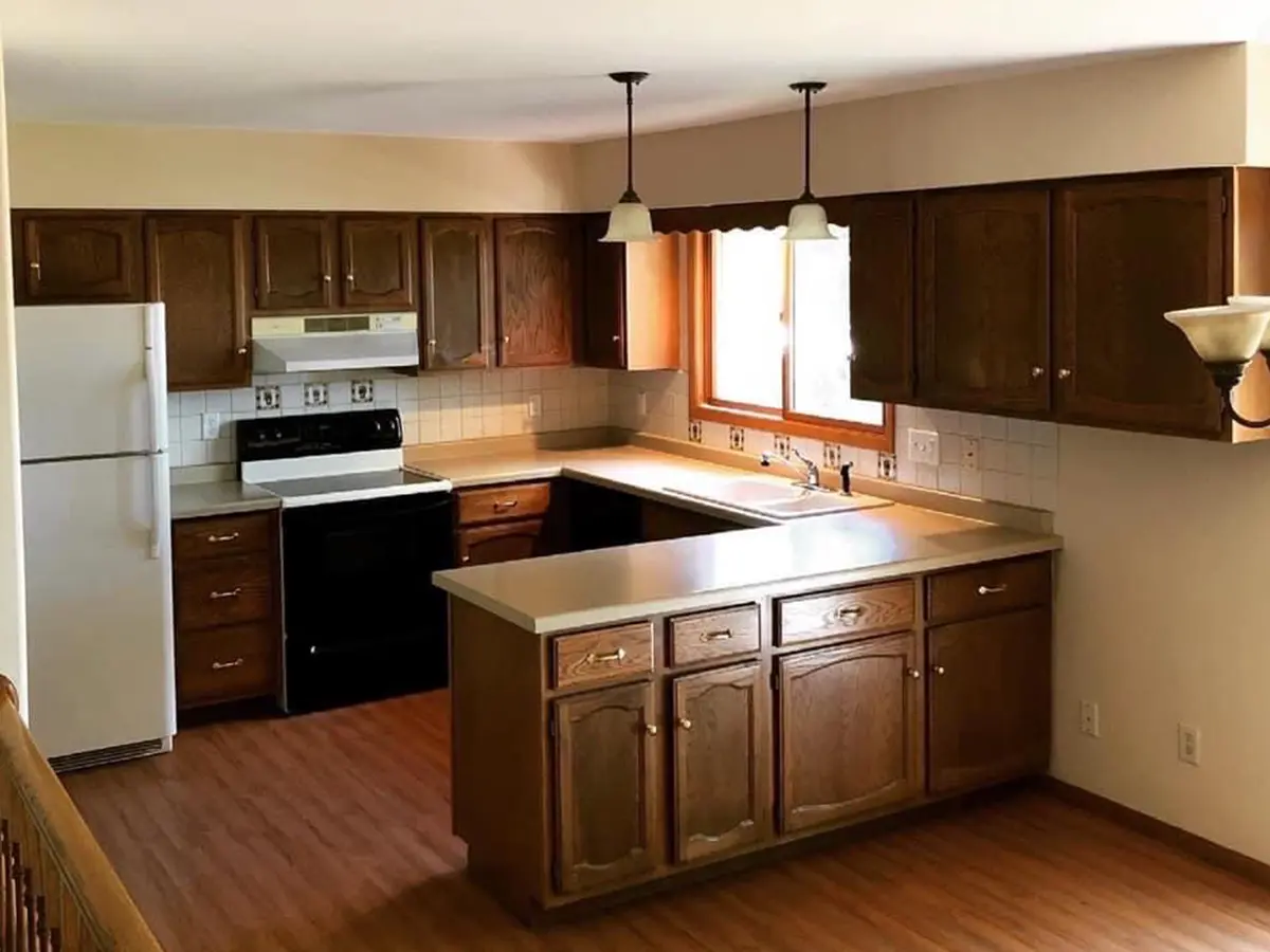 Dated wood cabinets and lighting fixtures in a kitchen with laminate flooring