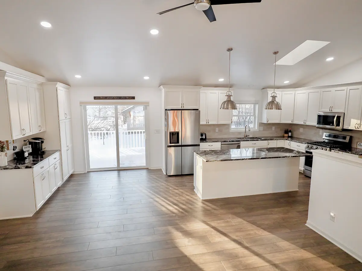 An open space kitchen with white kitchen cabinets, luxury vinyl plank flooring, and silver accents on hardware