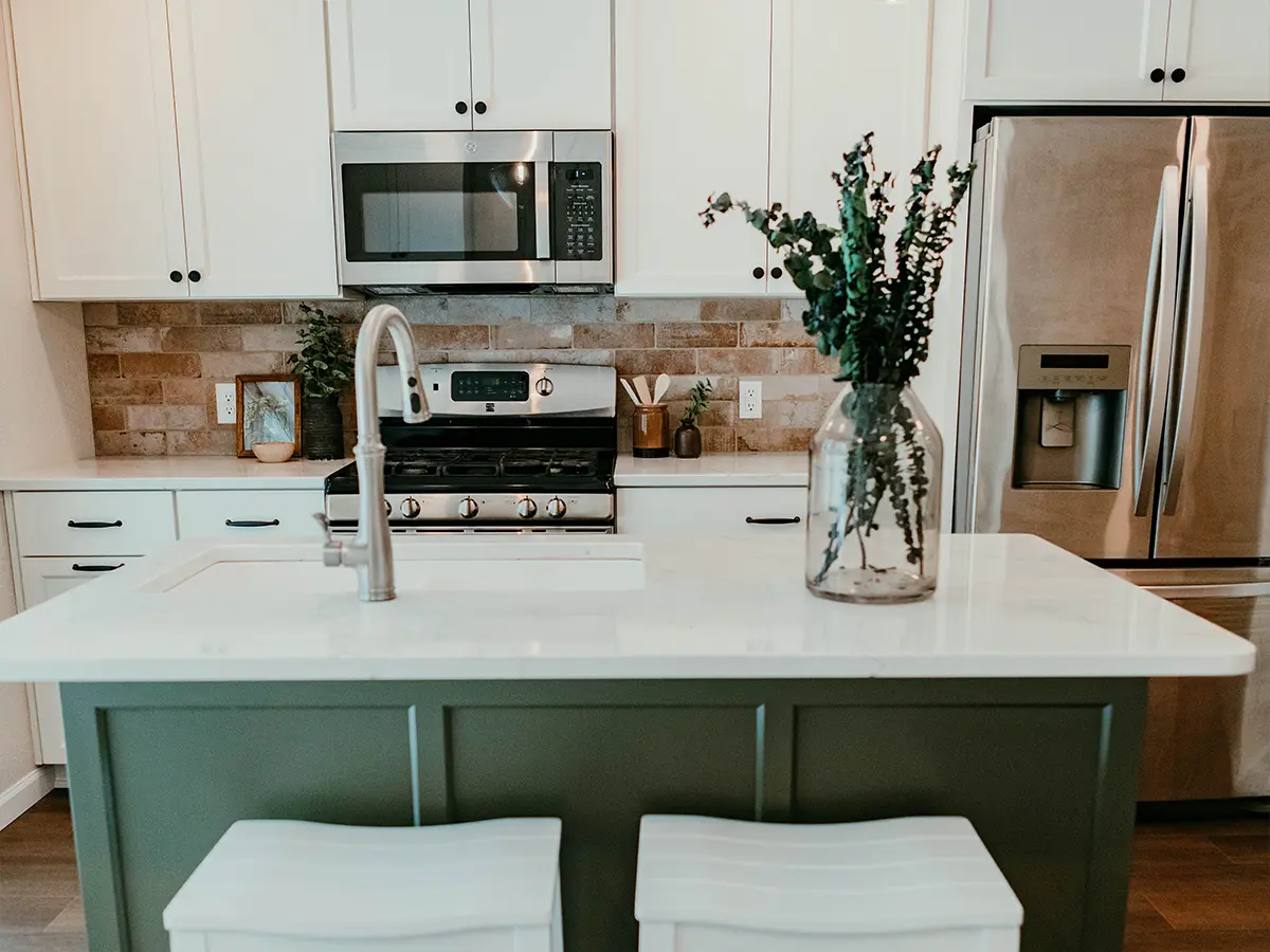 White kitchen cabinets with black pulls and knobs, LVP flooring, and a small, green island