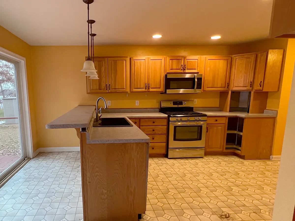 Wooden kitchen cabinets in a dated space with linoleum flooring