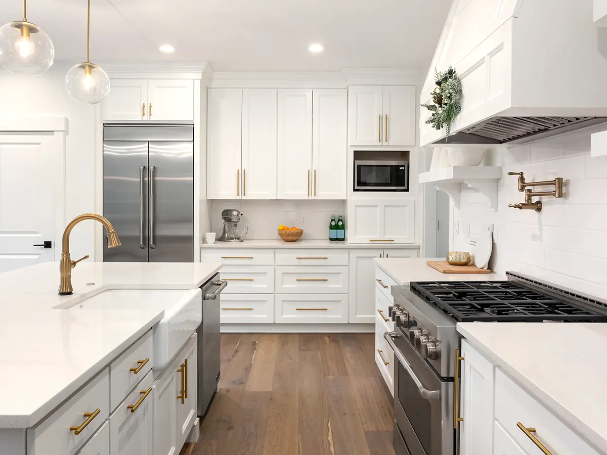 A kitchen with luxury vinyl plank flooring and white cabinets with golden hardware