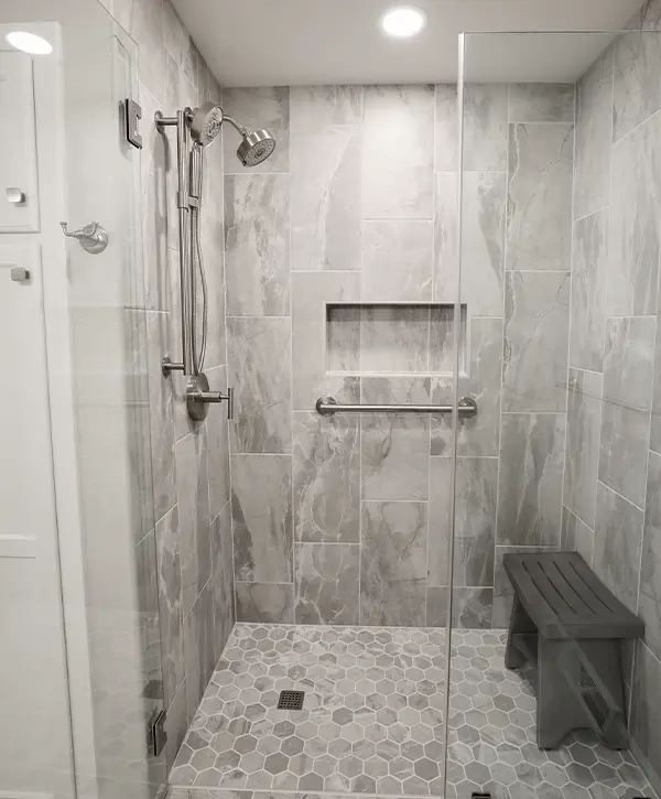A walk-in shower with a glass door and gray tile surround