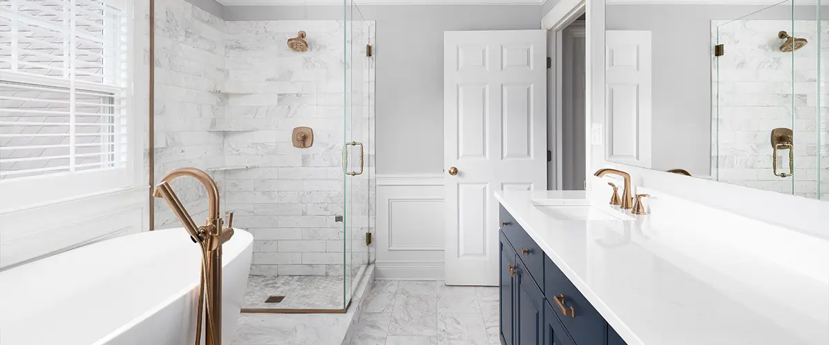 A beautiful bathroom with a blue vanity cabinet, standalone bathtub and shower, and gold faucets.