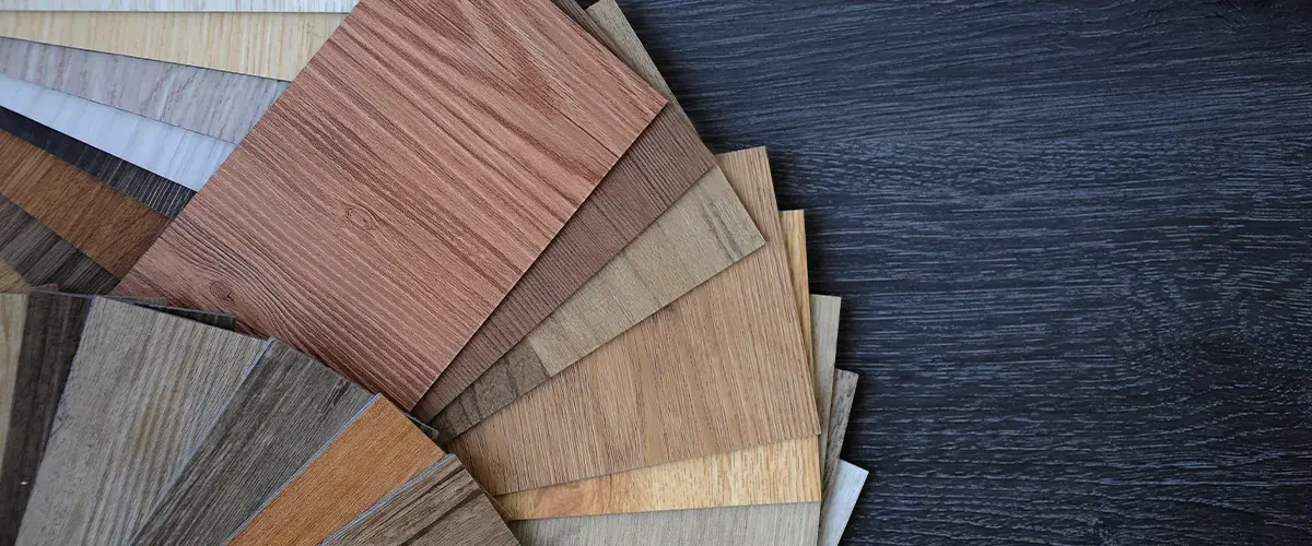 Assorted laminate flooring samples fanned out on a dark wood background, showcasing various wood grain patterns and shades.