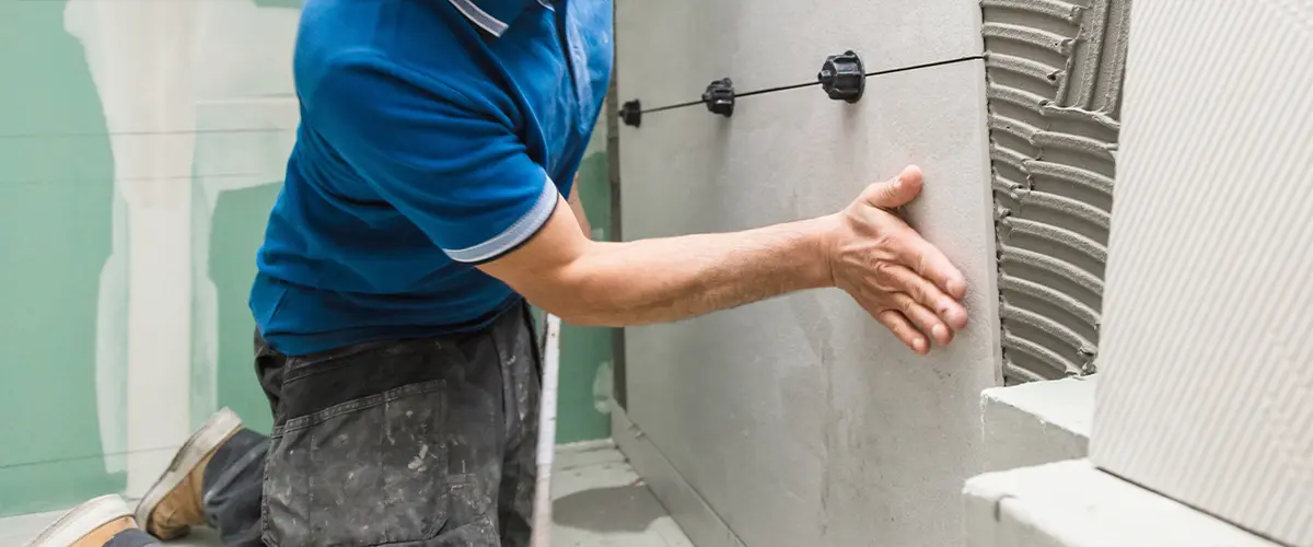 Worker installing ceramic tiles on a bathroom wall, emphasizing precision in home renovation projects.