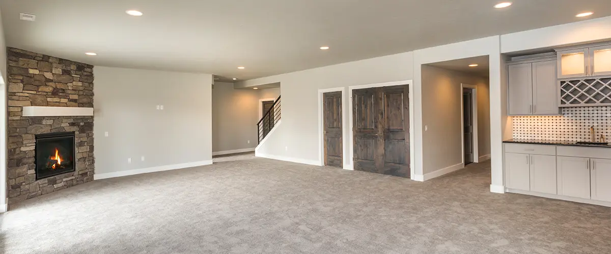 Spacious basement with stone fireplace, neutral carpet, built-in bar area, and wooden doors for modern home design.