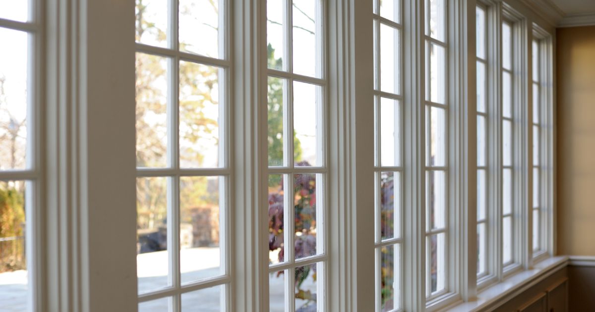 A row of elegant sunroom windows with white trim, allowing natural light to brighten the interior while offering a view of the outdoor landscape