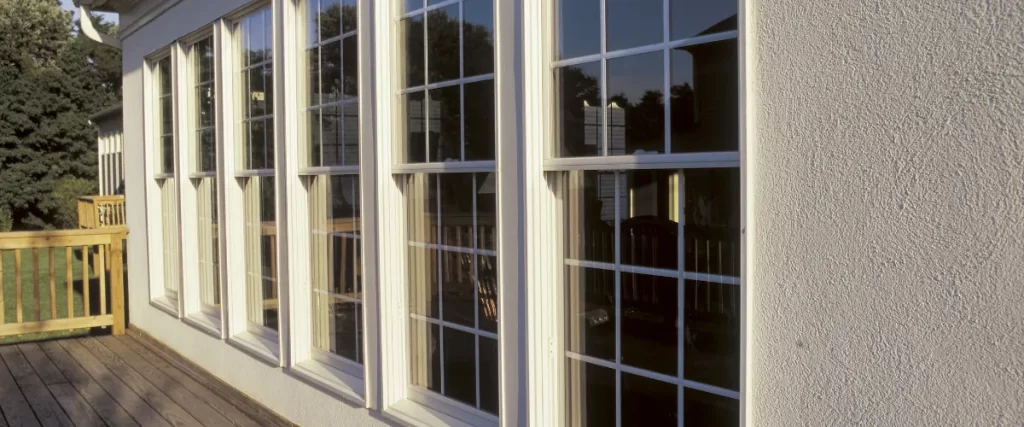 A row of large sunroom windows reflecting the surrounding deck and trees, allowing natural light into the home’s interior.