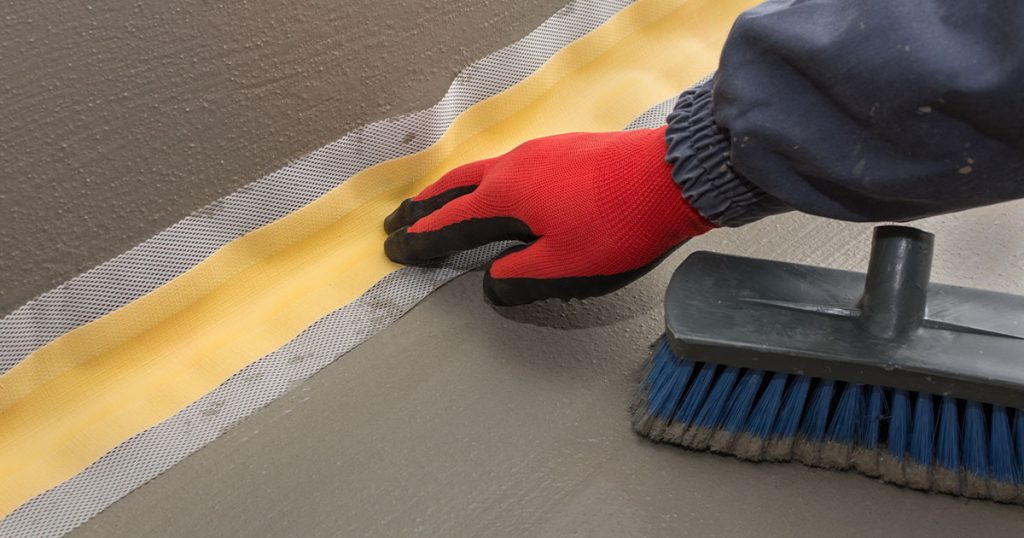 Worker-installing-waterproof-membrane-tape-at-floor-and-wall-joint-for-foundation-sealing-and-water-protection