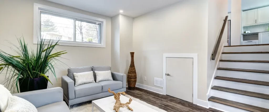A small basement living space with a couch, coffee table, large decorative vase, and a small window.