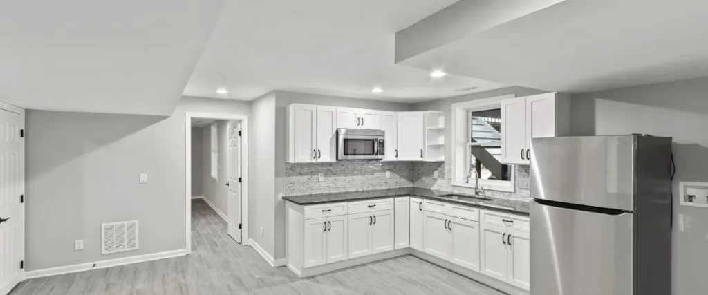 A bright basement kitchen with white cabinetry, granite countertops, and stainless steel appliances (selected).