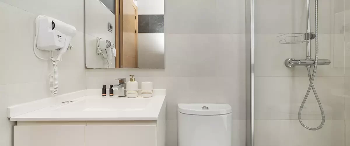 A small bathroom with a walk-in shower with a stone floor, a white cabinet with a sink, a wall-mounted hairdryer