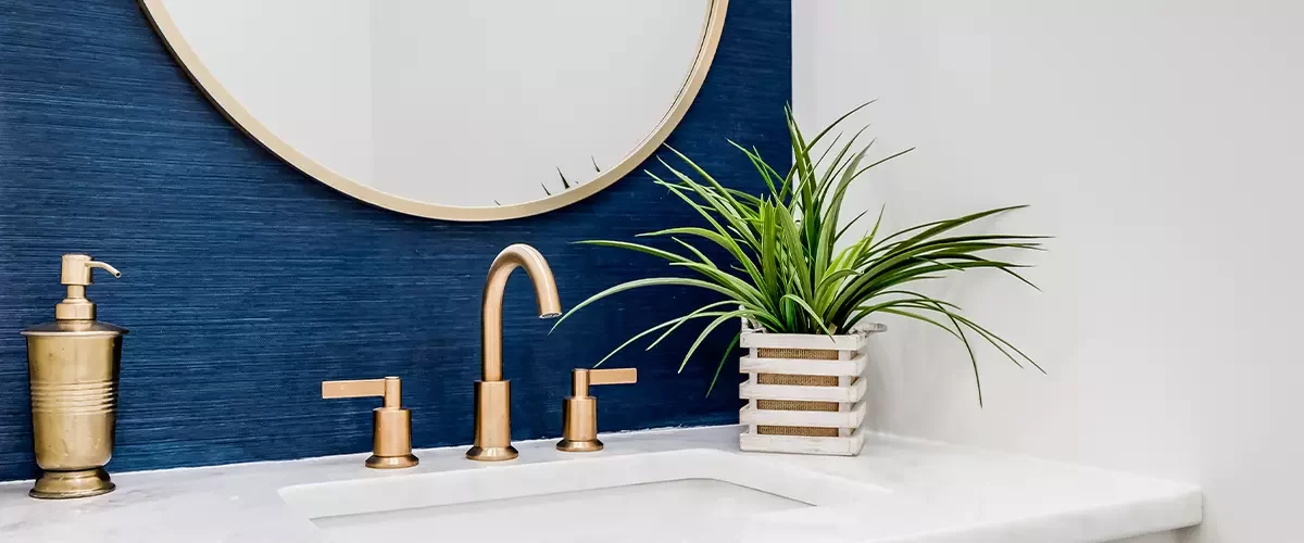 A small bathroom with blue wallpaper, gold hardware, and a white marble counter top.