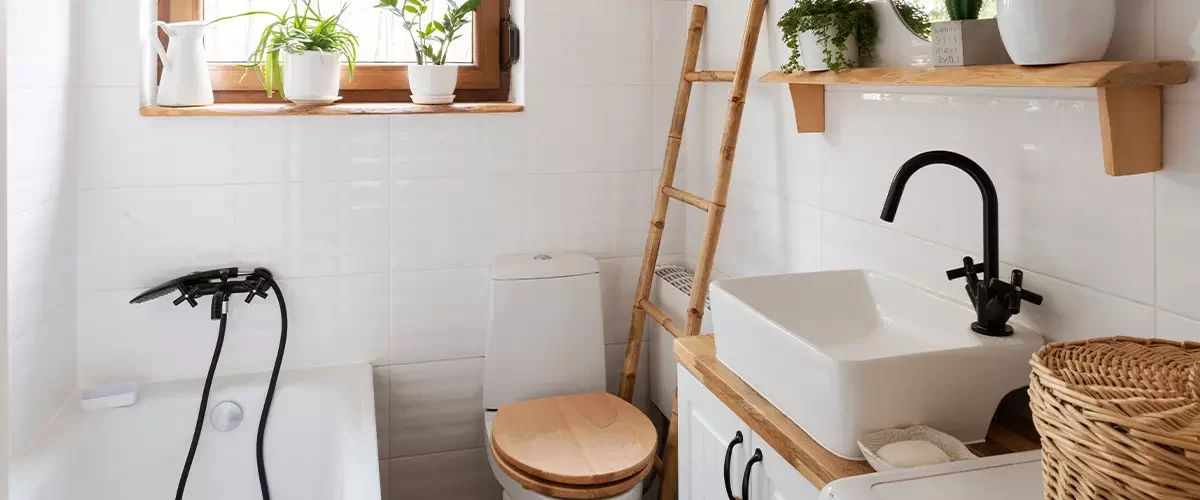 Small bathroom in a cottage in rural style with bath, toilet, stylish sink, wood, round mirror and plants. White interior in hotel spa.